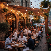 People dining outdoors at a restaurant with string lights and brick walls.